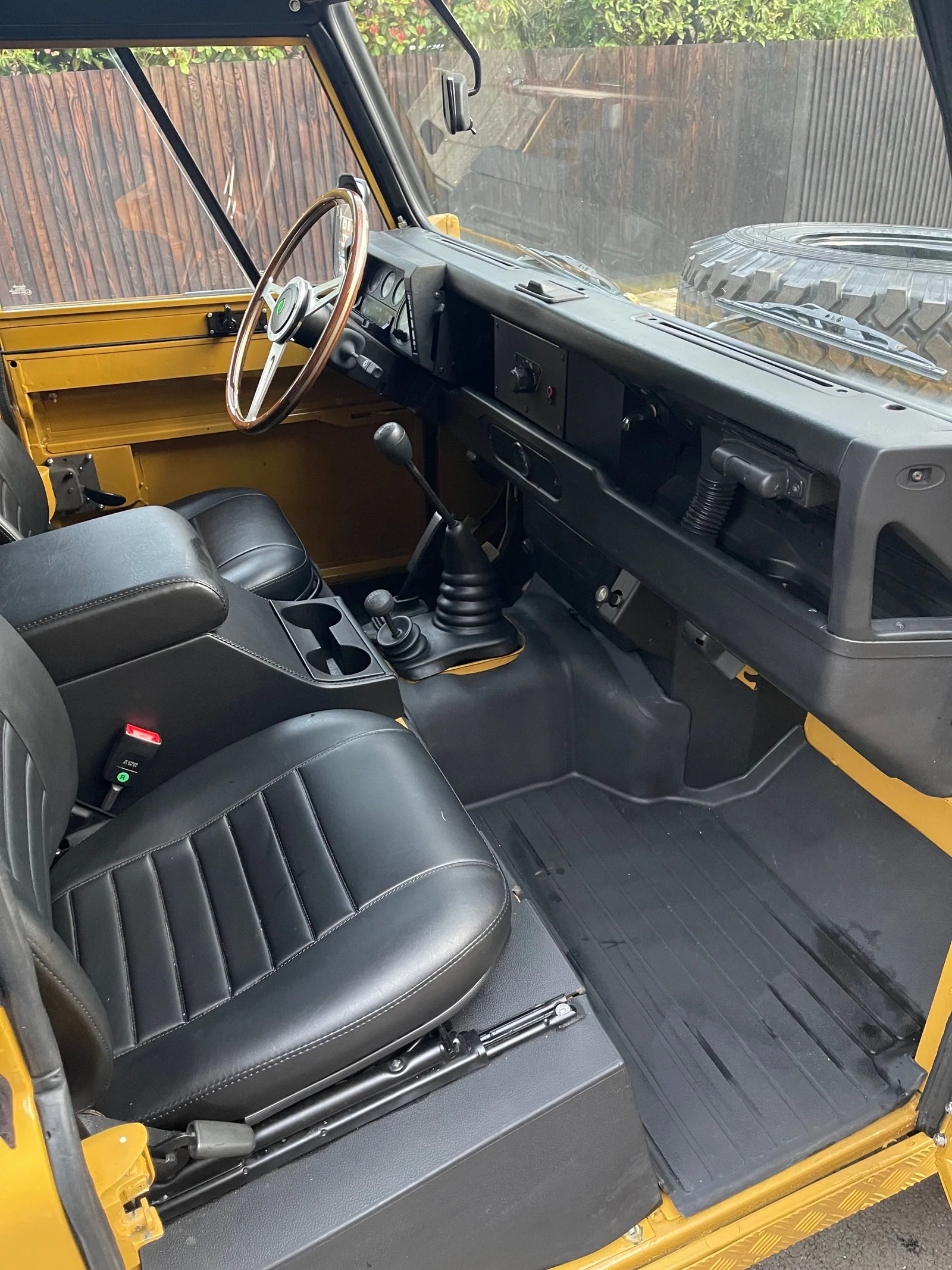 Defender front cabin with black seats, manual transmission and wooden steering wheel