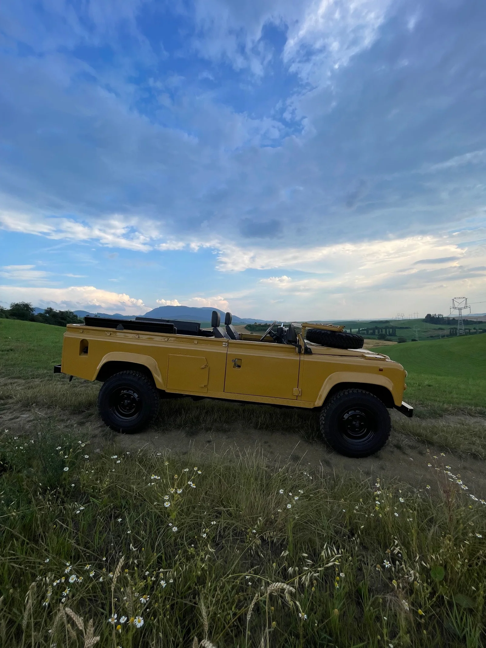 Full side profile of the open-top Defender 110 in countryside